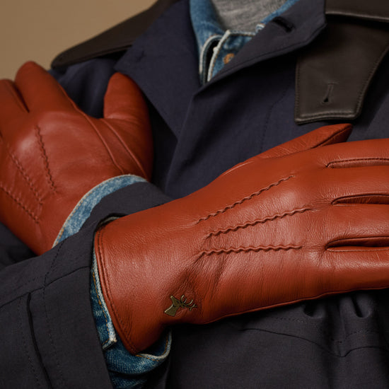 Men's cognac leather glove close-up with blue cuff lining and stitched seams