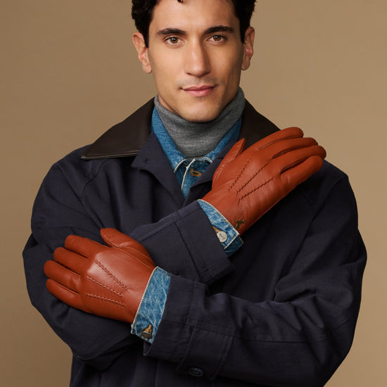 Men's cognac leather gloves with blue lining, arms crossed in front of coat
