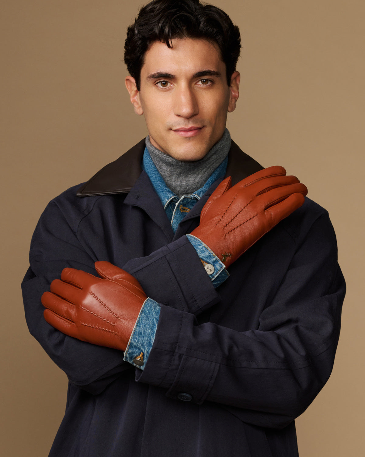 Men's cognac leather gloves with blue lining, arms crossed in front of coat