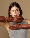 Cognac leather below-elbow gloves close-up, textured surface and fitted seams