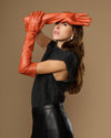 Orange leather gloves with long cuffs; touchscreen fingertips shown while hands are raised