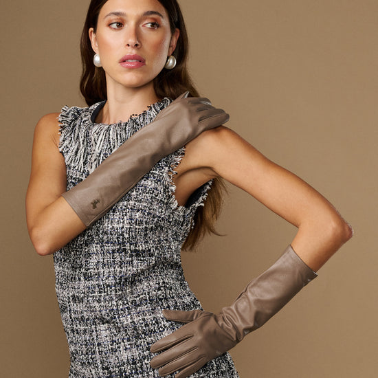 Taupe below-elbow leather gloves, front view on model arms, slim cuff and finger seams.