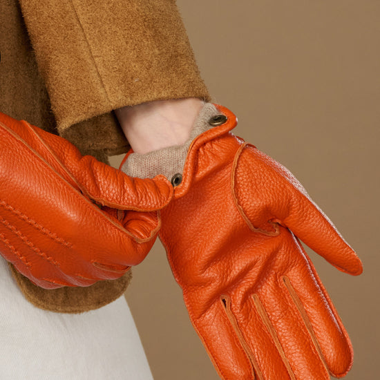 Orange leather glove with buttoned cuff and stitched panels, soft lining visible at wrist