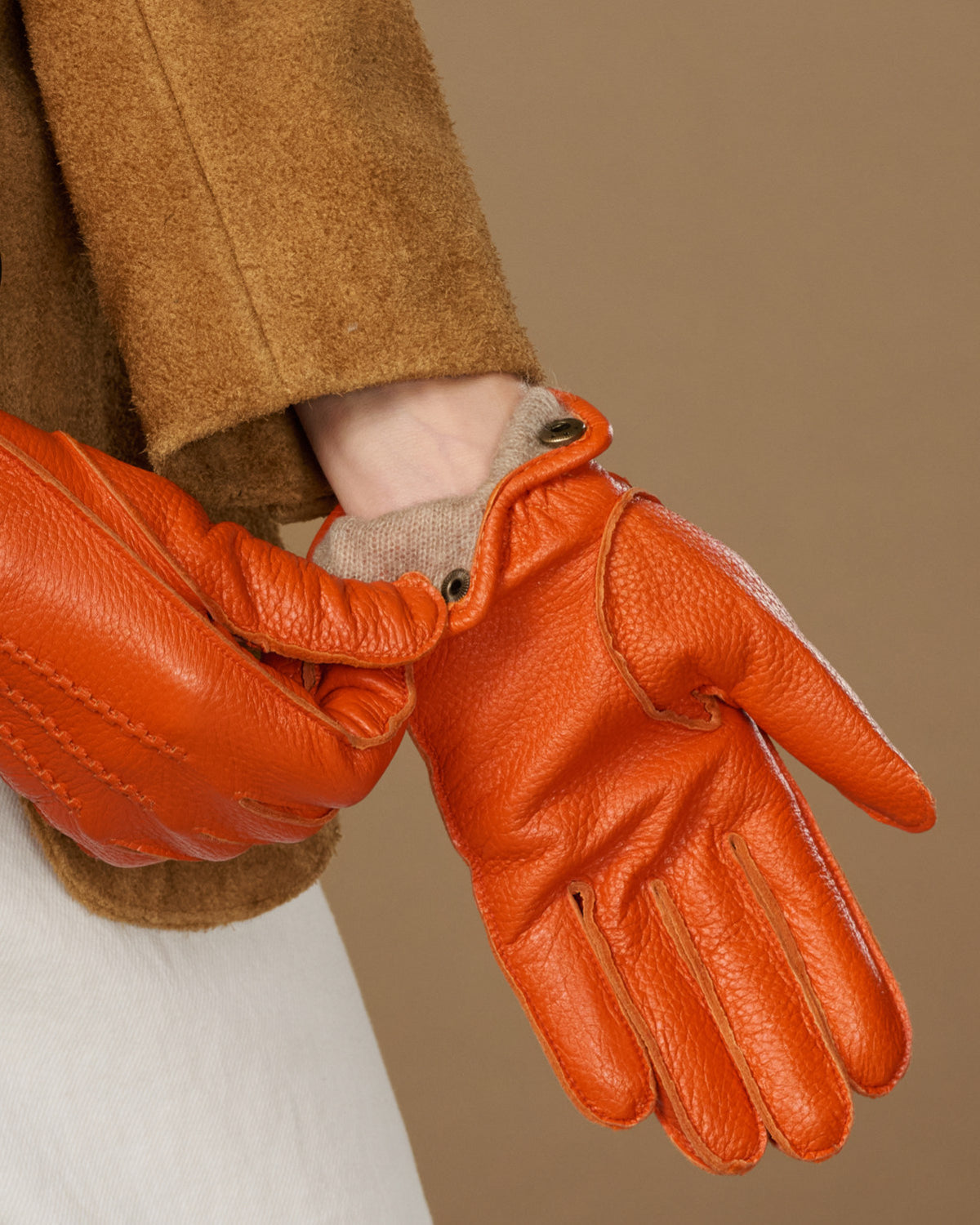 Orange leather glove with buttoned cuff and stitched panels, soft lining visible at wrist