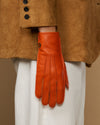Orange leather glove with soft lined cuff and stitched fingertips, hanging from sleeve